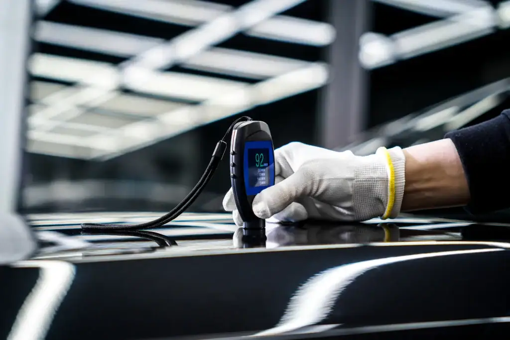 Main gantée mesurant l'épaisseur de peinture avec une jauge électronique